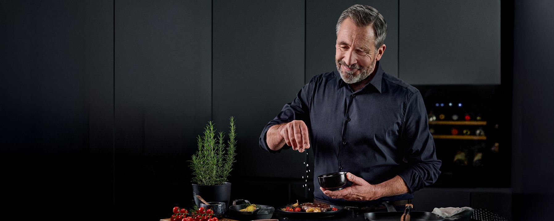 Person seasoning a dish in a black baking dish with a pink salz mill on a dark kitchen counter